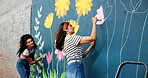Women, teamwork or friends painting on wall for mural, drawing flowers or community service at building. Artist, creative or girls with brush for floral decoration, renovation or project for design 