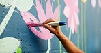 Person, hand or painting on wall art for mural, creativity or community service at building. Artist, paintbrush or outdoor with color for floral decor, creative process or flower for aesthetic design