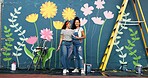 Outdoor, friends and women with wall art, smile and help for community service, confident and creative. Mural, happy and people with paintbrush for decoration, flowers and volunteers in Canada