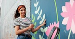 Mural, artist and woman with smile, portrait and proud of decoration for wall art, creative and paintbrush. Happy, painter and flowers for design in neighbourhood, outdoor or community project in USA