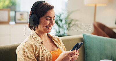 Buy stock photo Woman, phone and headphones on sofa, smile and texting in home with streaming, audio and relax in lounge. Girl, smartphone and happy with mobile app for listening to music on couch at apartment