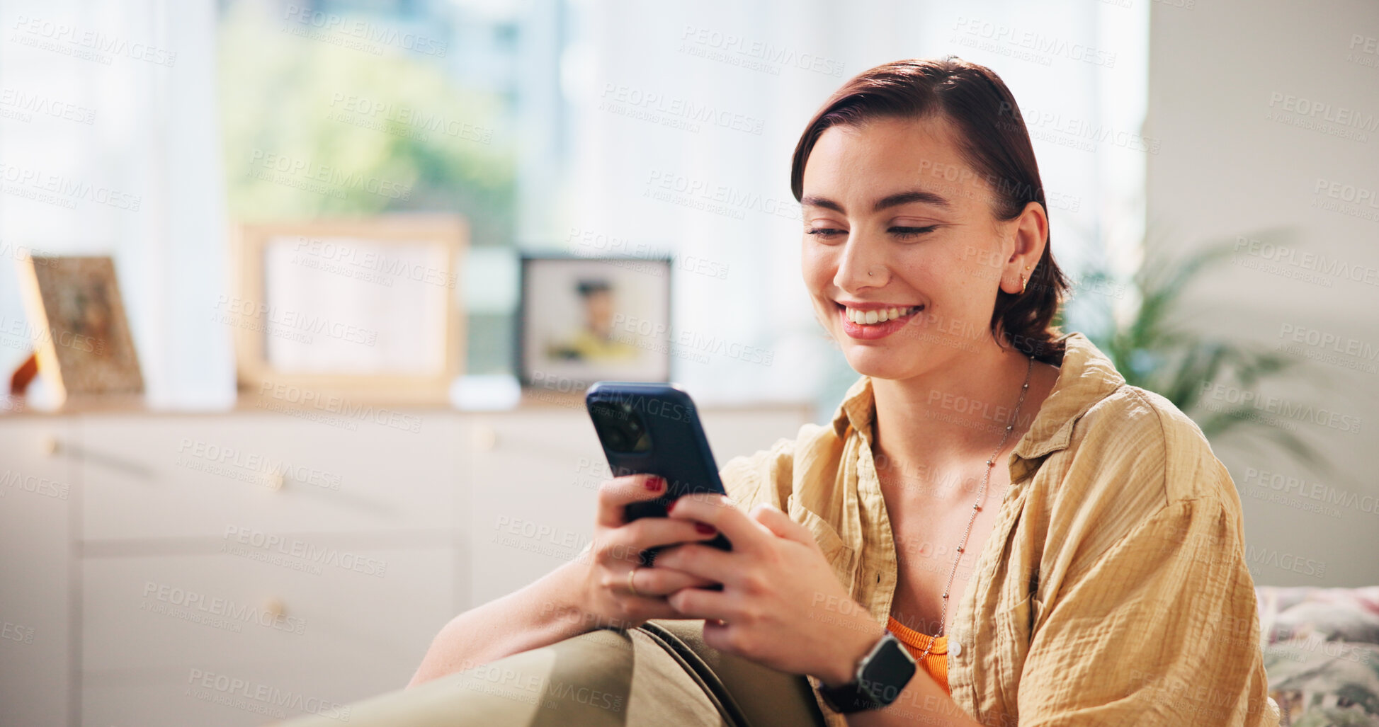 Buy stock photo Woman, happy and phone on sofa, relax and texting with funny meme in living room at apartment. Girl, person and smartphone with mobile app, comic video and smile on couch with social media in home