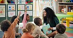 Reading, question and teacher with children in classroom for education, books and creative. Growth, kindergarten and academy with woman and kids at school for youth, hands raised or child development