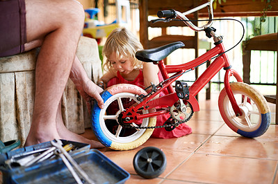 Buy stock photo Father, kid and repair bicycle in home with help, support and DIY fix for child development. Man hands, young daughter and bike in living room for remove training wheels, growth and family bonding
