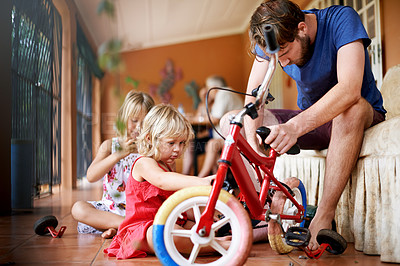 Buy stock photo Man, children and repair bicycle in home with help, support and DIY fix for kid development. Father, young daughters and bike in living room for remove training wheels, growth and family bonding