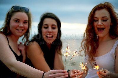 Buy stock photo Girls, friends and celebration with sparklers at beach for social gathering, summer break and holiday adventure. Dusk, happy people and fireworks by ocean for party event, bonding or vacation travel 