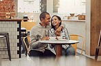 Loving young man sitting with his arm around his girlfriend while sitting at a table and having coffee in a cafe. Loving mixed race couple talking and laughing while on a date