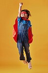 Adorable little asian boy wearing a mask and a cape while pretending to be a superhero against an orange studio background. Cute happy boy pretending to be a character for halloween