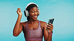 Phone, dance and black woman with headphones in studio for listening to music, radio or album. Happy, cellphone and African person streaming on mobile app with audio tech for song by blue background.