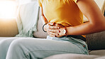 Home, woman and hands with pain for stomach, menstrual cramps and discomfort on sofa in living room. Closeup, female person and ache on couch for colon inflammation, abdomen health and constipation