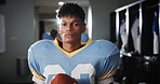 Man, football player and ball in locker room for portrait, protective gear and confident for tournament. National sport, serious and athlete in cloakroom for fitness, game and competition in USA