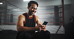 Man, phone and happy at gym by boxing ring with chat, contact and texting for notification at training center. Person, athlete or fighter with smartphone, smile and social media at martial arts club