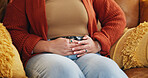 Hands, pain and person with stomach cramps, constipation and sick with irritable bowel syndrome on sofa. House, illness and woman with pelvic inflammatory disease, menstruation and touch of belly