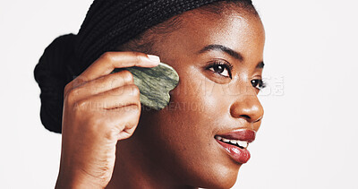 Buy stock photo Beauty, skincare and black woman with gua sha in studio for lymphatic drainage, blood circulation or puffiness reduction. Self care, girl and face with jade stone for radiant skin on white background