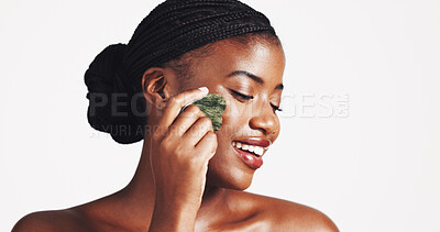 Buy stock photo Cosmetics, skincare and black woman with gua sha in studio for lymphatic drainage, natural beauty or self care. Dermatology, girl and smile with jade stone for radiant skin on white background mockup