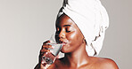 Woman, drinking water and towel for skincare in studio with glow, detox and self care by background. African girl, model and glass with liquid for gut health, wellness and beauty with cosmetics