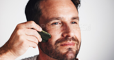 Buy stock photo Skincare, gua sha and man in studio, cosmetics and dermatology on white background. Person, space and model with jade stone, self care and shine with wellness, beauty and facial treatment with glow