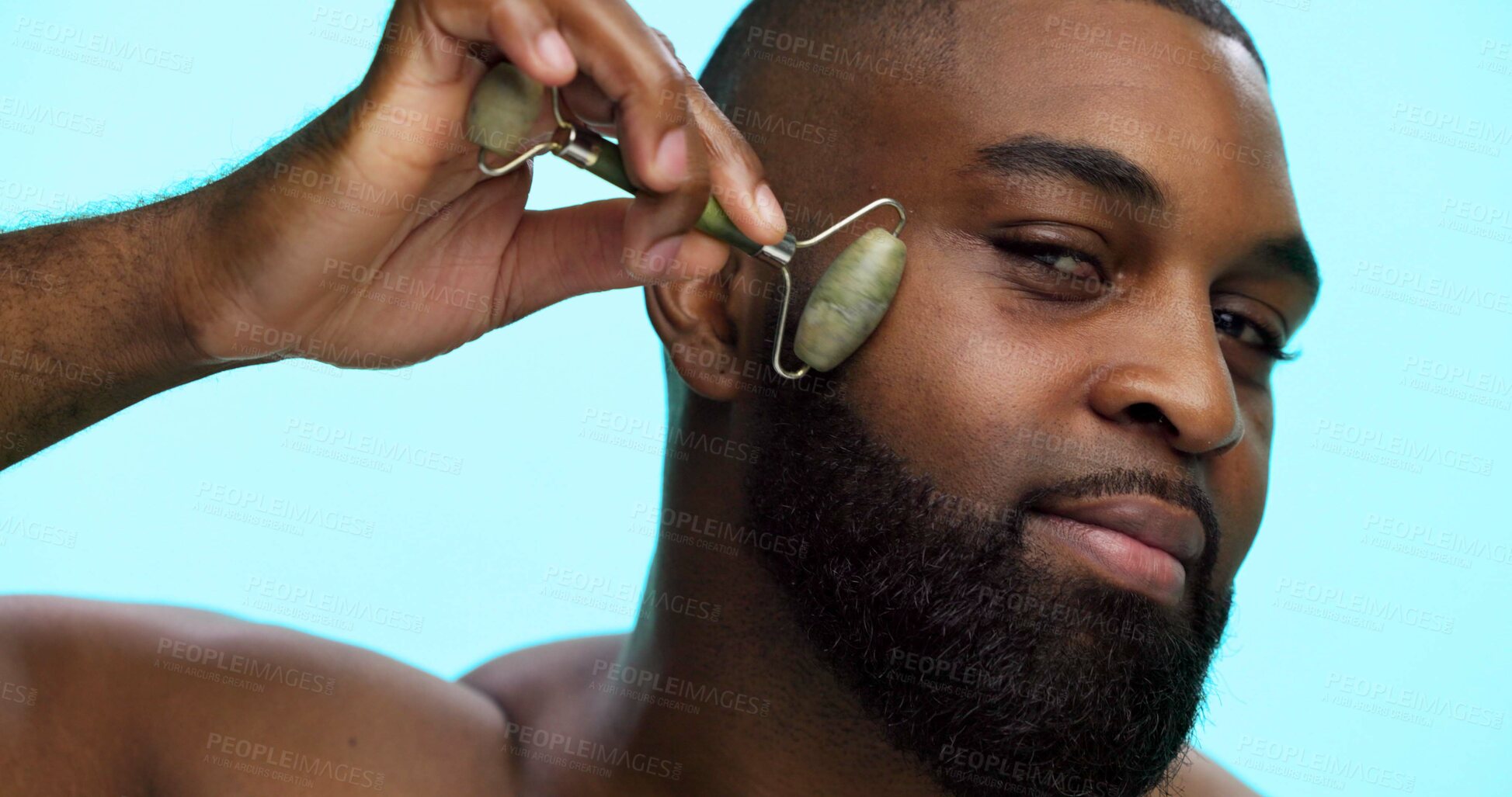 Buy stock photo Black man, jade roller and natural skincare in studio, facial massage or lymphatic drainage to reduce puffiness. Healthy glow, stone tool and cosmetic care portrait for dermatology on blue background