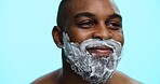 Face, foam and shaving with black man in studio, cosmetic care and product with skincare on blue background. Soap, cream or facial maintenance for hair removal, smile and grooming for hygiene