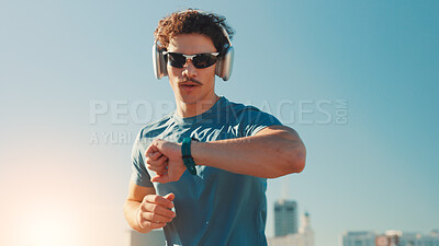 Buy stock photo Man, fitness and checking watch with headphones in city for workout app or tracking performance. Active, male person or runner with wristwatch for music, calories or running exercise on space in town