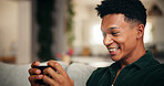 Gaming, phone and smile with man on sofa for esports streaming, cyber sport league and relax. Happiness, gamer app and subscription platform with person in living room of home for online tournament