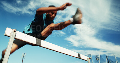 Man, athlete and jump by hurdle for fitness competition, challenge and contest at sports field. Low angle, sprint obstacle and sky with blur for speed, leap and performance for marathon event