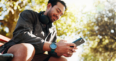 Buy stock photo Phone, fitness and man on park bench for break, training stats and text message online in low angle. Mobile, smile and athlete resting outdoor with app for workout schedule or track health progress