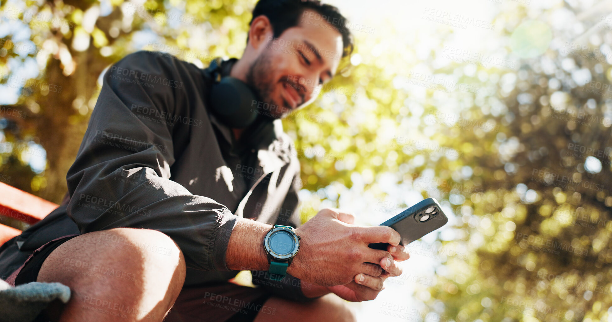 Buy stock photo Phone, fitness and man on park bench for break, training stats and text message online in low angle. Mobile, smile and athlete resting outdoor with app for workout schedule or track health progress