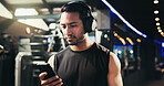 Man, phone and headphones at gym for training, streaming and check stats for exercise routine. Person, smartphone and listening to music, subscription and mobile app with click at fitness club