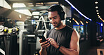Man, phone and headphones at gym for texting, streaming and check stats for exercise routine. Person, smartphone and listening to music, subscription and mobile app with training at fitness club
