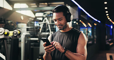Buy stock photo Man, phone and headphones at gym for texting, streaming and check stats for exercise routine. Person, smartphone and listening to music, subscription and mobile app with training at fitness club