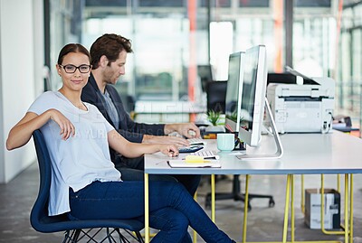 Buy stock photo Portrait of a woman with her male colleague sitting at computers in a large office