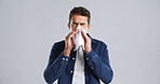 Sick man, sneeze and blowing nose with tissue in studio for cold, flu or sinus on a gray background. Male person, model or influenza with cough or allergy for hayfever or illness on mockup space