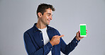 Happy man, pointing and phone with green screen for advertising on a white background. Male person, model or user with smile, mobile smartphone display or chromakey for marketing app on mockup space