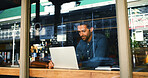 Coffee shop, laptop and business man by window for typing report, proposal and research. Restaurant, cafeteria and person on computer for internet, online project and review for freelance career