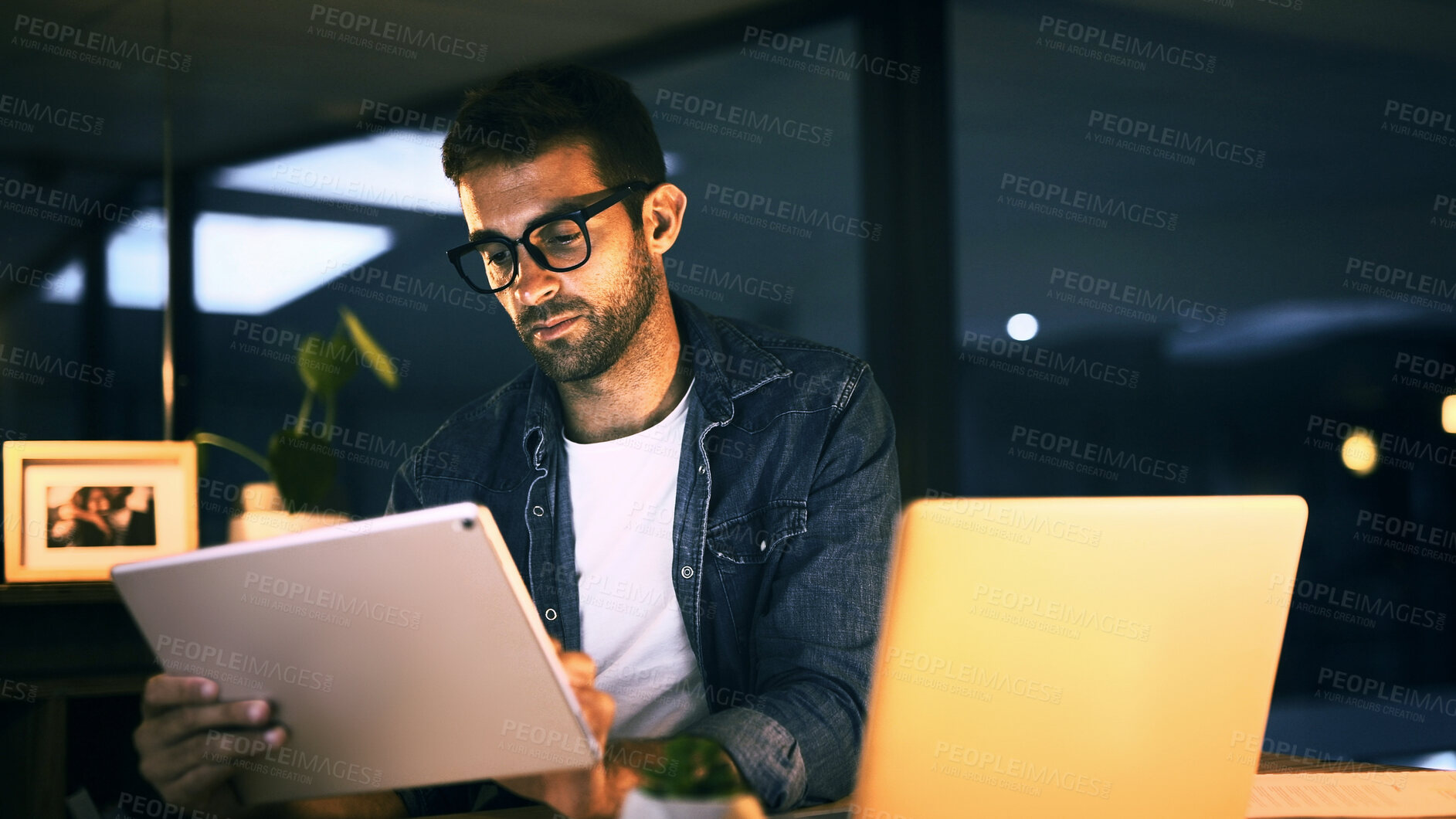 Buy stock photo Tablet, laptop and man in office at night with creative project with publishing online. Glasses, digital technology and magazine editor with computer for reading article, review deadline or workplace
