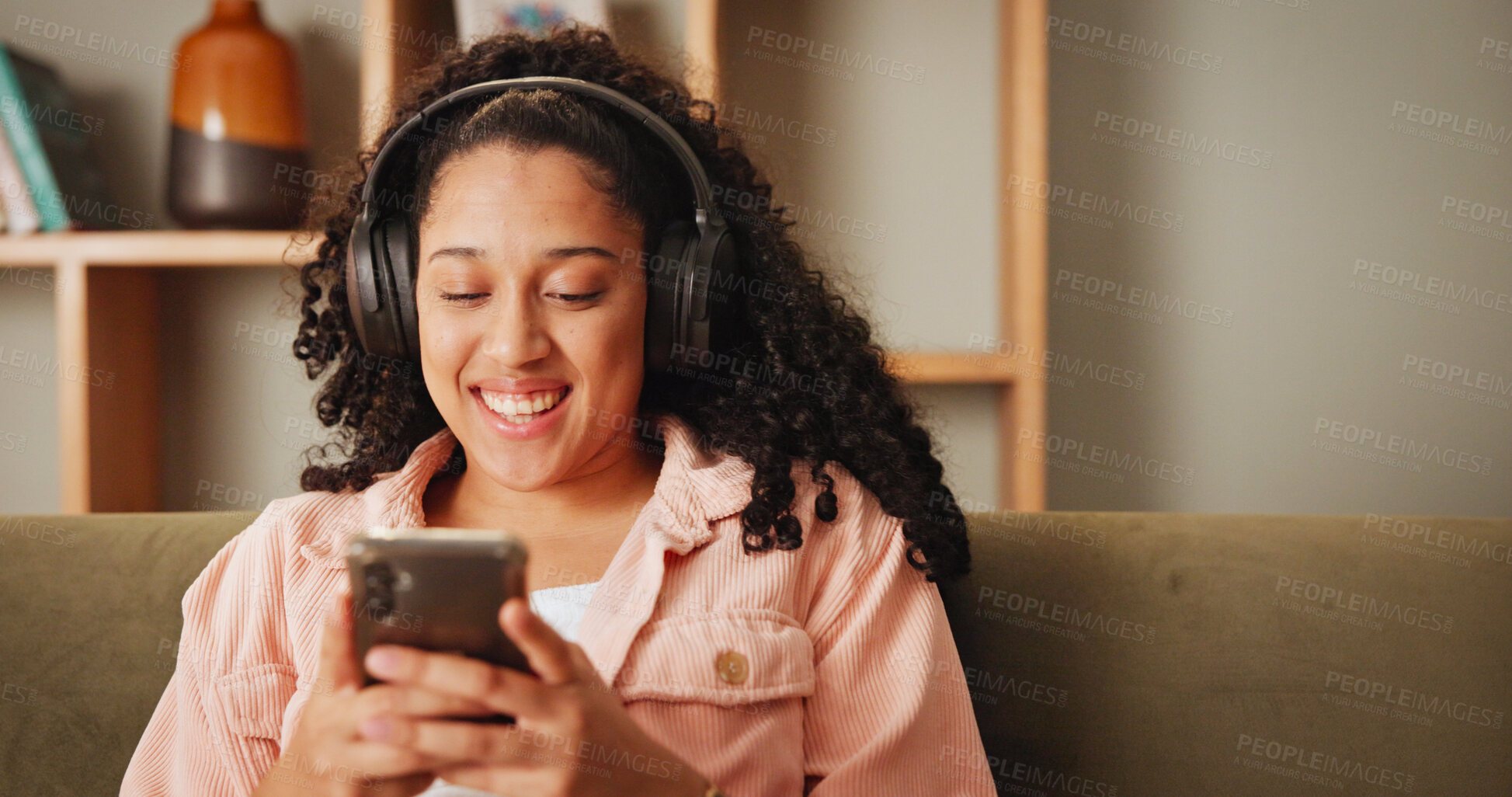 Buy stock photo Girl, phone and happy on sofa with headphones, texting and contact for funny chat in living room. Woman, smartphone and laugh with listening to music, streaming and social media on couch at apartment