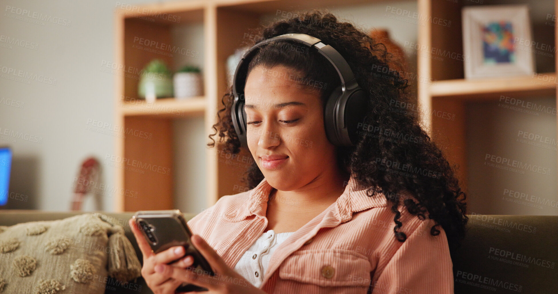 Buy stock photo Girl, phone and texting on sofa with headphones, smile and search for funny video in living room. Woman, smartphone and happy with listening to music, streaming and social media on couch at apartment