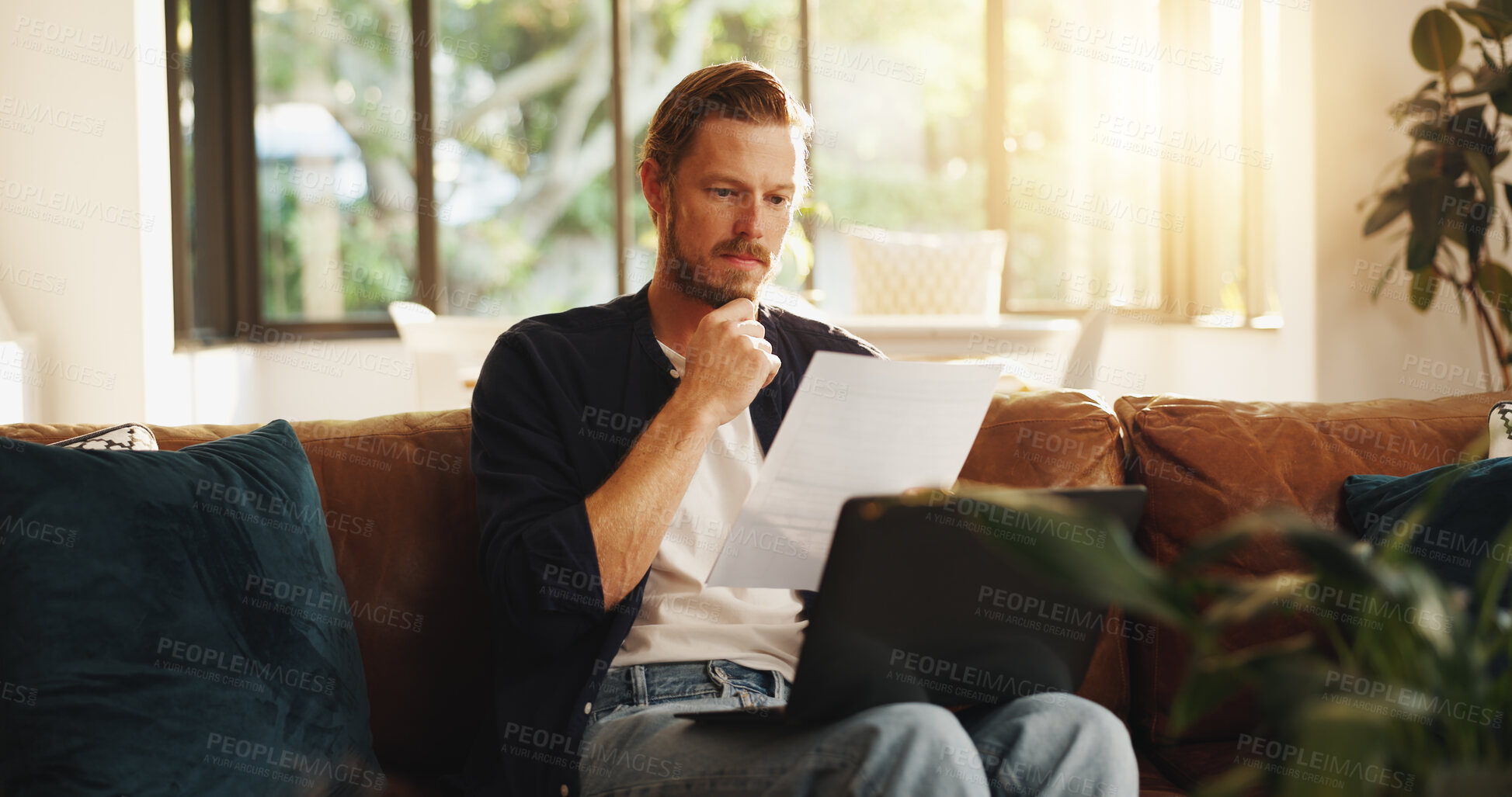 Buy stock photo Man, document and reading on sofa with laptop, writer and thinking for script draft in home. Person, editor and technology in living room for paperwork, networking and application with freelancer
