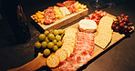 Charcuterie board, party and snacks on table in home with biscuits, cold meats and cheese for food. Catering, fruit and wooden plate with fresh ingredients and crackers for gourmet selection.