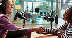 Podcast interview, host or guest with handshake in studio for welcome, talk show or radio broadcast. Media production, content creation and happy women with shaking hands for greeting and live stream