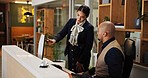 Man, woman and concierge with team at hotel with computer, point and discussion for booking info. People, mentor and receptionist with training by pc for hospitality internship with coach at lodge