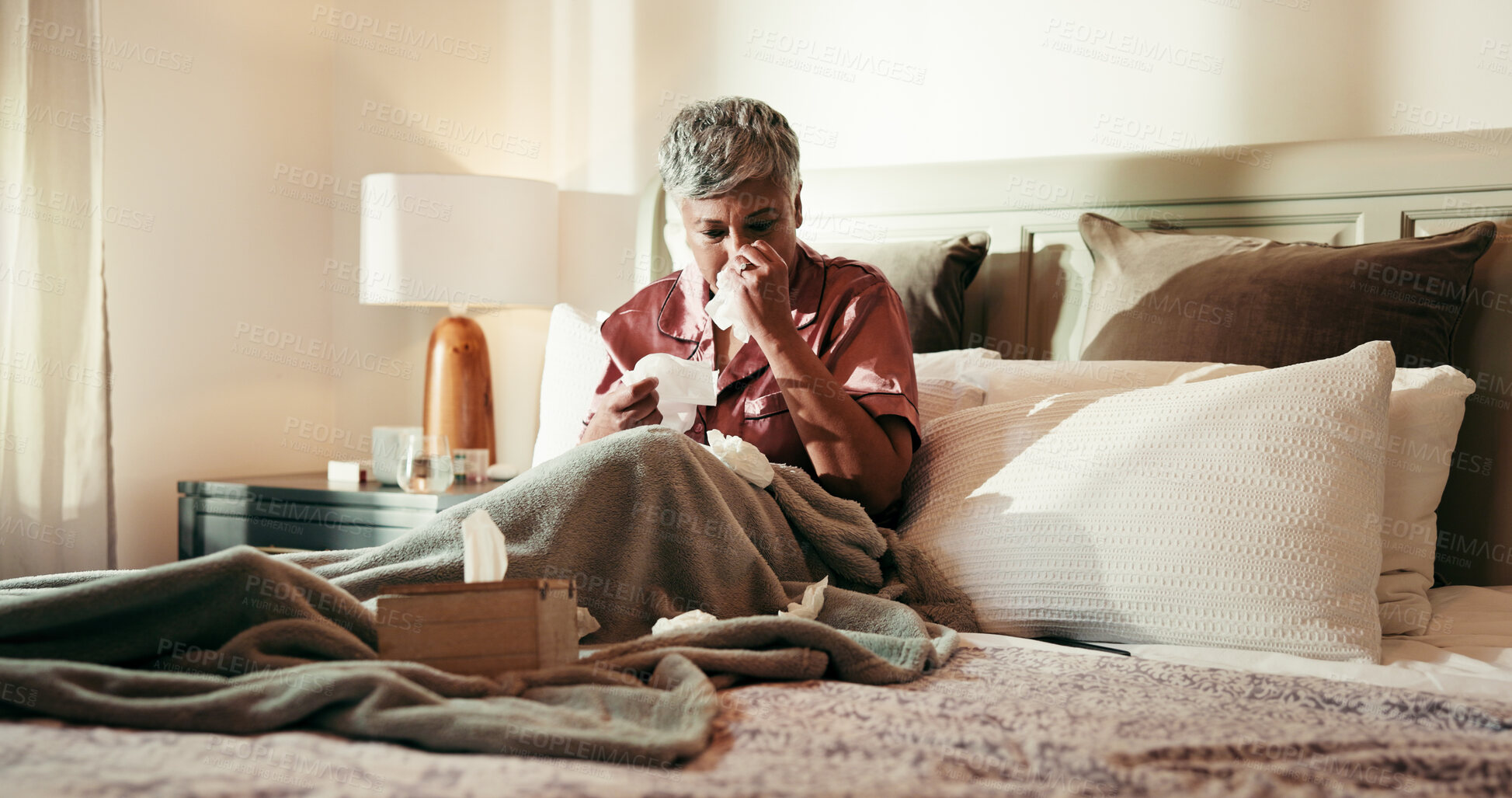 Buy stock photo Senior, sick woman and blowing nose on bed with tissue for influenza or viral infection at home. Female person, virus and cold with flu, sinus or hayfever in bedroom for germs, bacteria or sneeze
