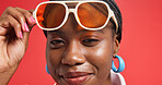 Black woman, portrait and sunglasses with makeup in studio for fashion on a red background. Face, female person or African model with smile or swag for beauty cosmetics, style or cool accessories