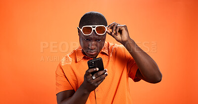 Buy stock photo Black man, phone and shocked in studio with chat, thinking and reading post on orange background. African person, smartphone and doubt with fake news, gossip and confused on social media with choice