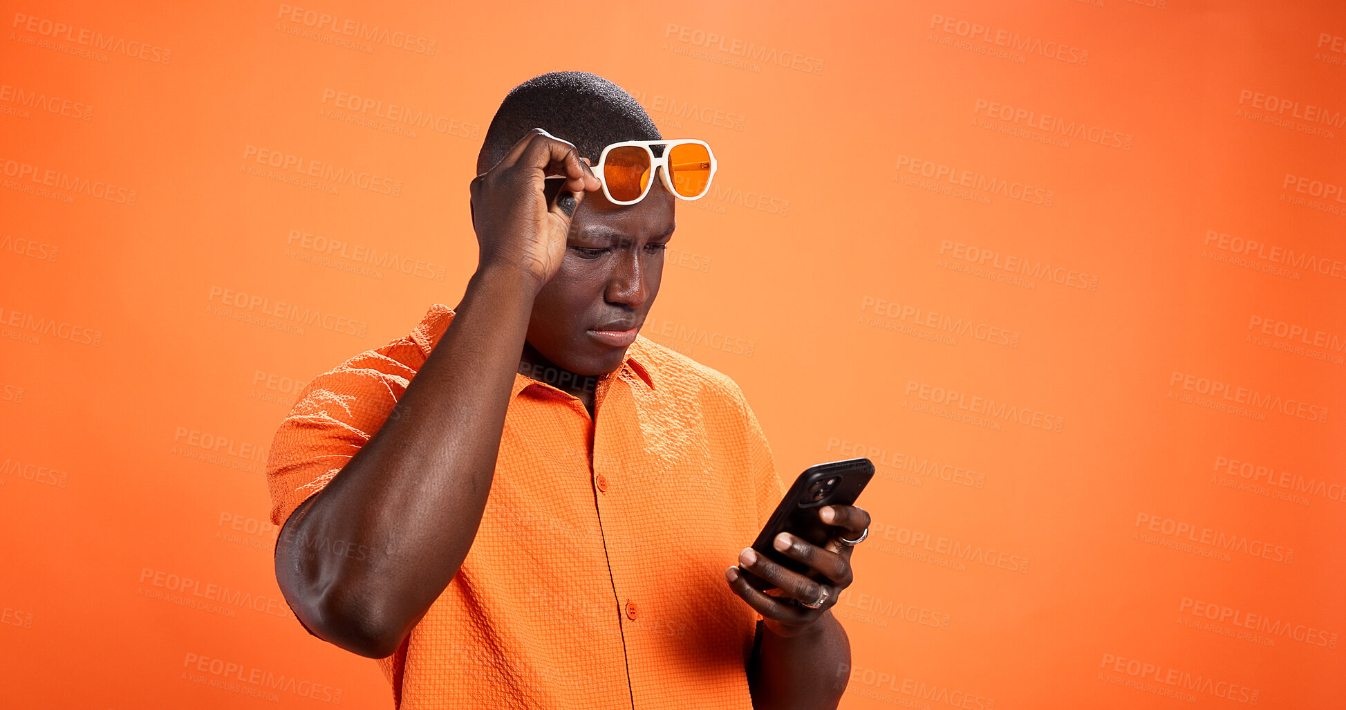 Buy stock photo Black man, phone and confused in studio with chat, thinking and reading post on orange background. African person, smartphone and doubt with fake news, gossip and scroll choice on social network