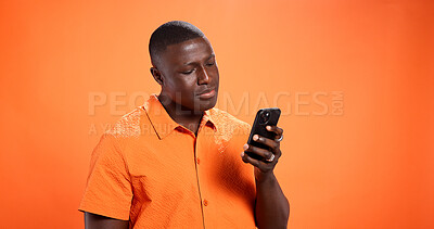 Buy stock photo Black man, phone and texting in studio with chat, thinking and reading post on mobile app on orange background. Person, smartphone and notification with contact, scroll and choice on social network