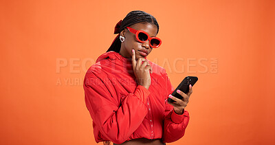 Buy stock photo Woman, phone and texting in studio with thinking, chat and reading post on app on orange background space. Black person, mobile and notification with contact, scroll and choice on social network