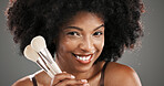 Makeup, brushes and portrait of black woman in studio for foundation, cosmetics and beauty products. Cosmetology, happy and person with tools for skincare, makeover and aesthetic on gray background