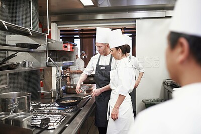 Buy stock photo Chef, teamwork and people with frying pan in kitchen, catering service and prepare food for fine dining. Professional, cooking and man training woman, saute and cook add oil to meat in restaurant.